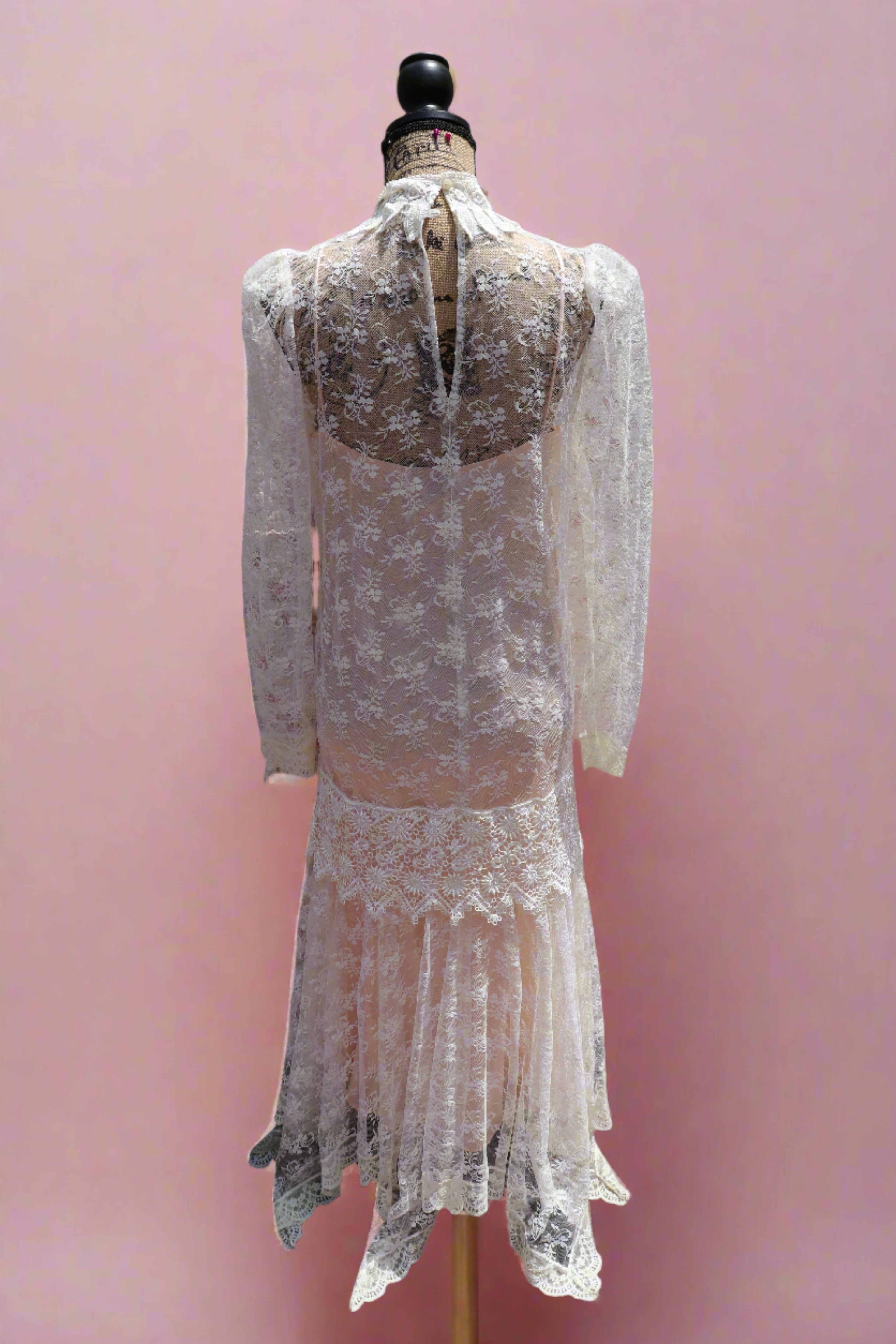 Back view of the samantha dress - a mashup of 1920s glamour and 1980s flair from Jessica McClintock. This white drop-waist puff shoulder turtleneck lace dress is laid over a delicate peach silk slip. Two for the price of one! Upgrade your wardrobe with this unique, versatile piece.