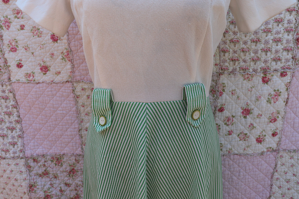 Introducing the Mabel Dress: a playful 1970s throwback. This white terry cloth dress features a green pinstripe skirt and collar, with a small cutout and cream buttons on the neck for added cuteness. Perfect for hitting the courts this summer!