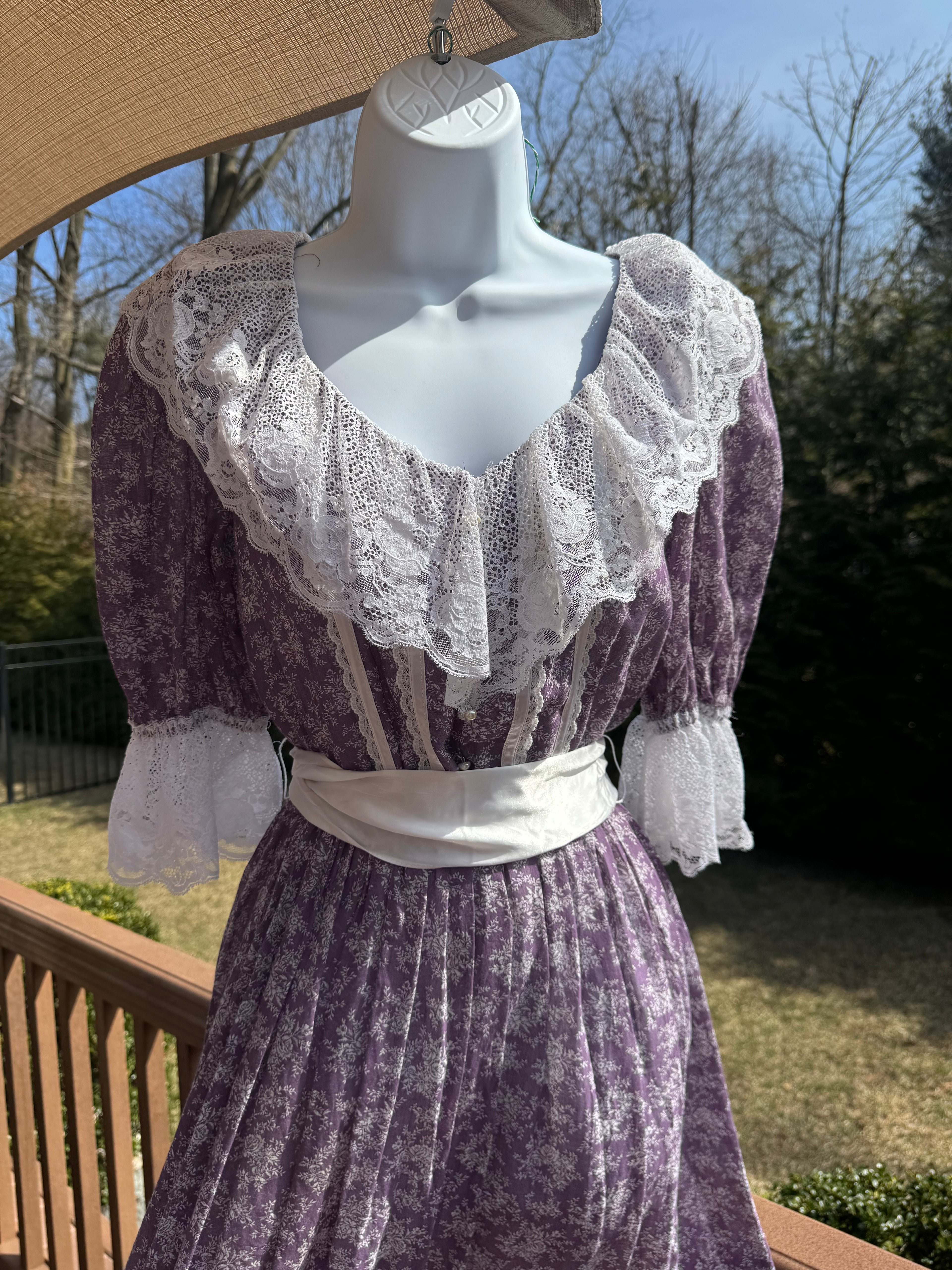 Float like a fairy in the faye dress! This gorgeous purple 1970s Gunne Sax dress is adorned with a dainty white floral pattern and crisp white lace trim. The button front adds an extra touch of unique fun and the attached white ribbon belt adds an extra touch of glamor. Marked as a size 9.