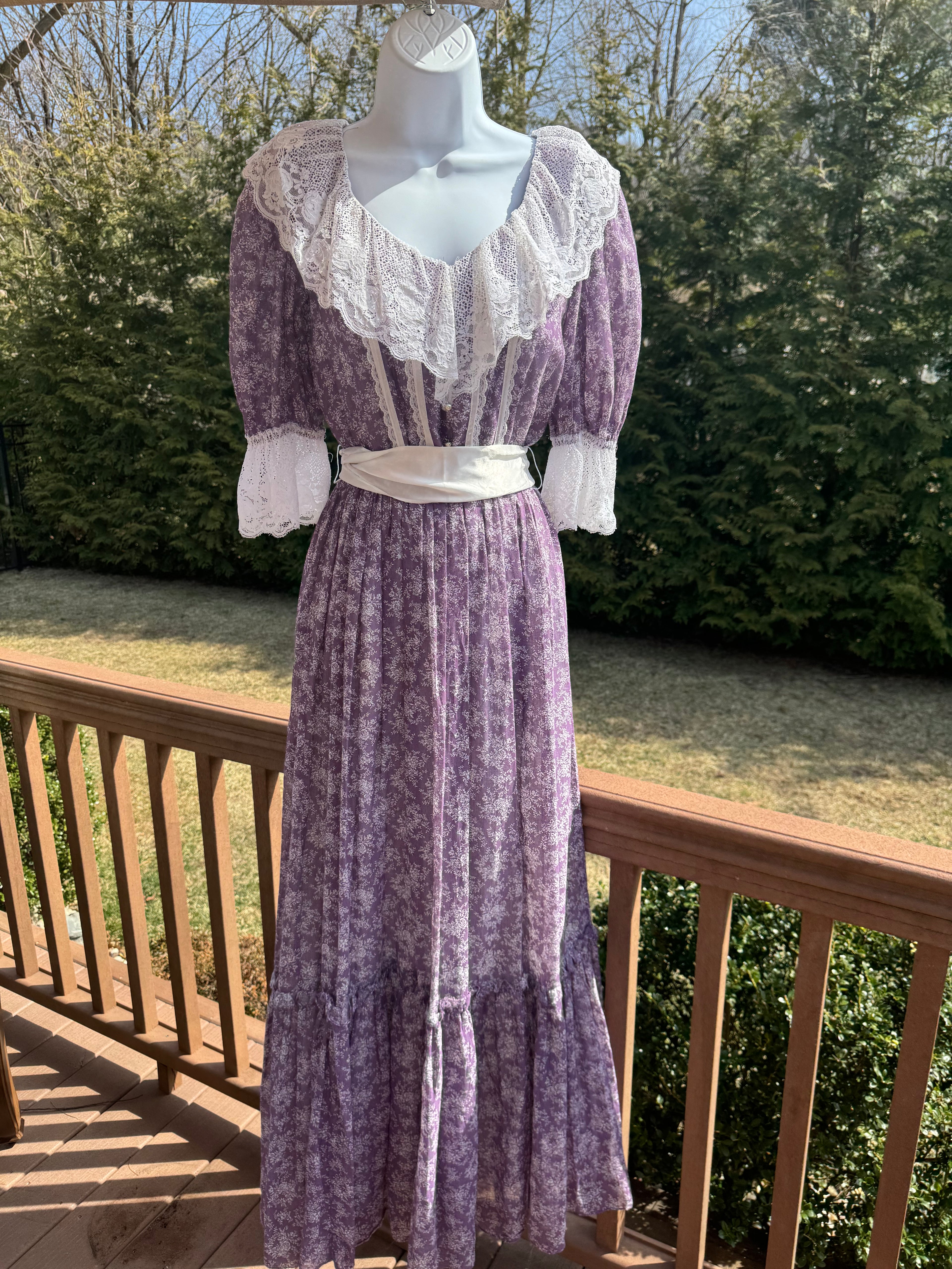Float like a fairy in the faye dress! This gorgeous purple 1970s Gunne Sax dress is adorned with a dainty white floral pattern and crisp white lace trim. The button front adds an extra touch of unique fun and the attached white ribbon belt adds an extra touch of glamor. Marked as a size 9.