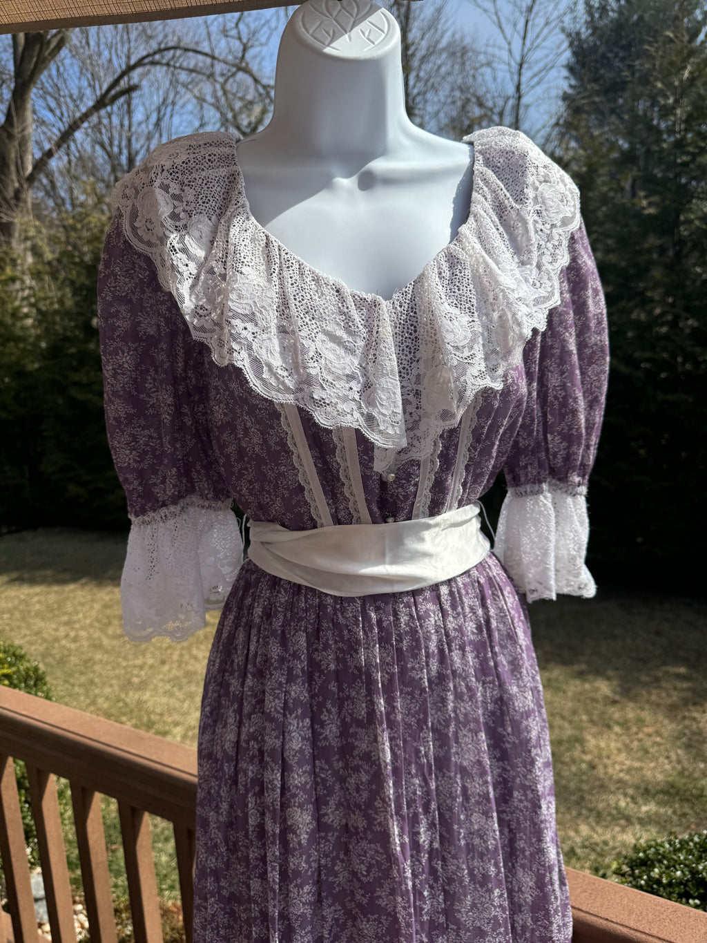 Float like a fairy in the faye dress! This gorgeous purple 1970s Gunne Sax dress is adorned with a dainty white floral pattern and crisp white lace trim. The button front adds an extra touch of unique fun and the attached white ribbon belt adds an extra touch of glamor. Marked as a size 9.