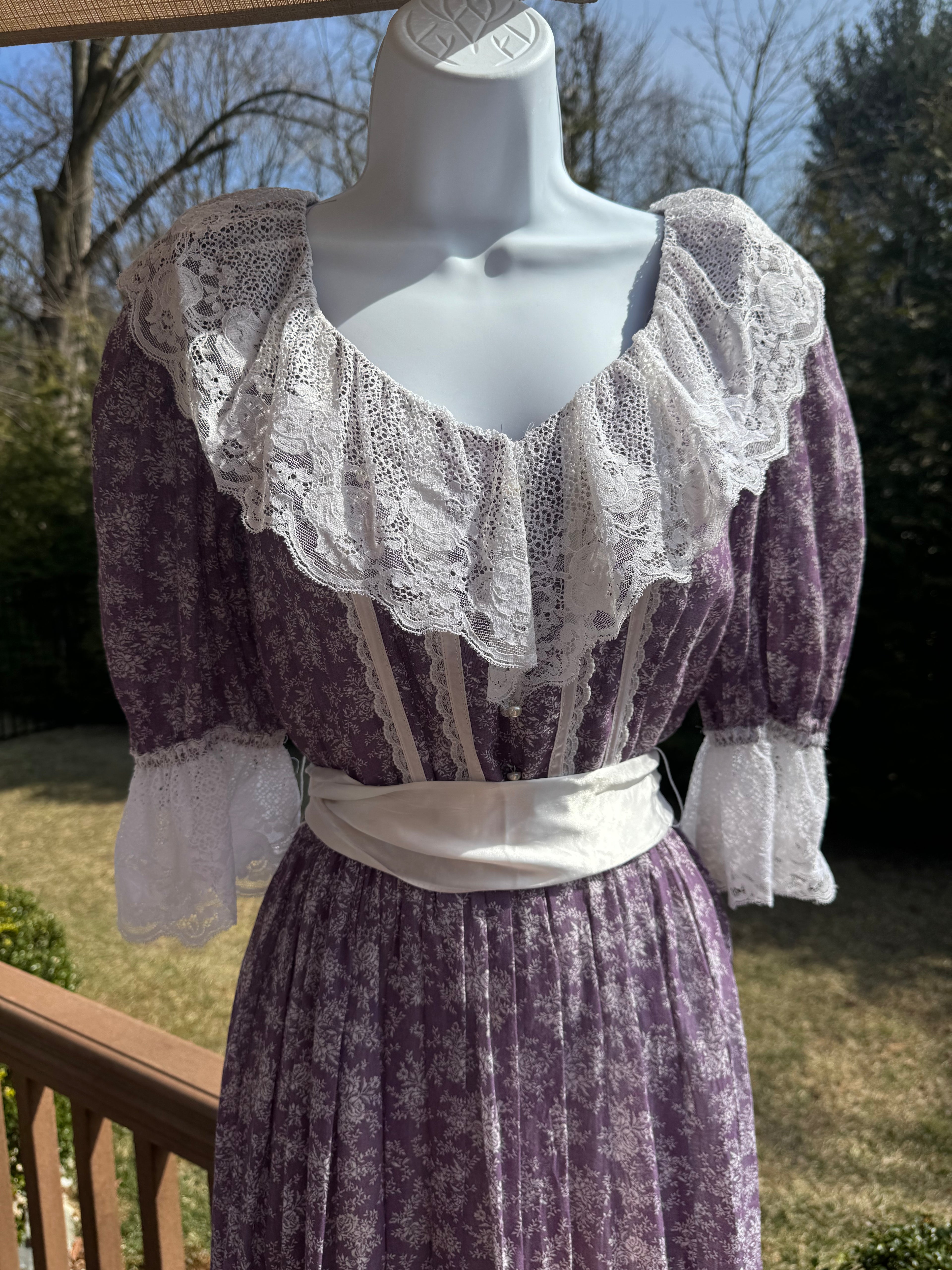 Float like a fairy in the faye dress! This gorgeous purple 1970s Gunne Sax dress is adorned with a dainty white floral pattern and crisp white lace trim. The button front adds an extra touch of unique fun and the attached white ribbon belt adds an extra touch of glamor. Marked as a size 9.