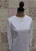 A white long sleeve shift dress with eyelet detailing and a small snap button on each wrist, displayed on a mannequin against a floral patterned background.